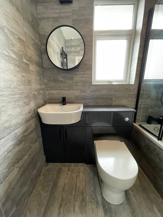 Refurbished grey bathroom with vanity unit, round mirror and black brassware