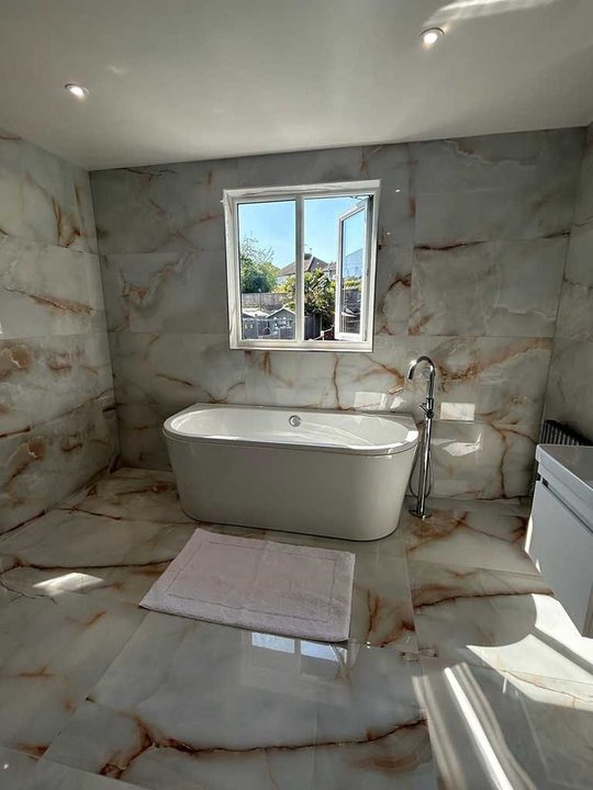 Freestanding bath and floor standing tap in a bathroom tiled floor to ceiling in onyx effect porcelain