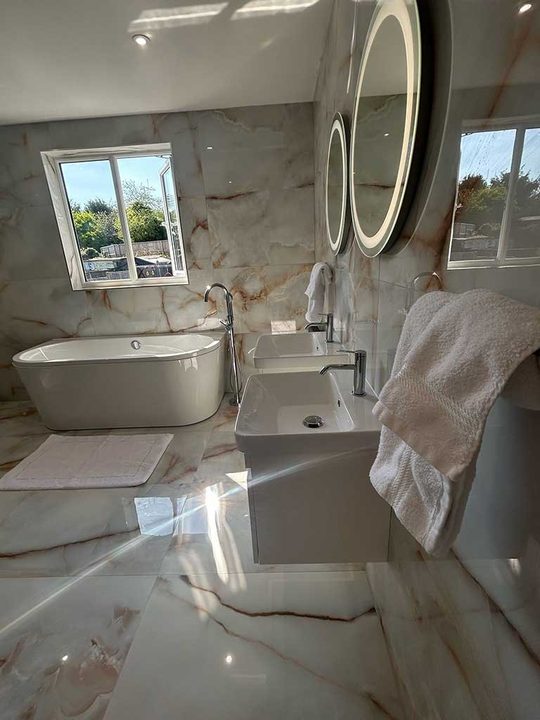 Twin basins and illuminated round mirrors in a refurbished bathroom with onyx effect tiling