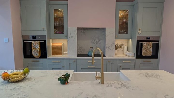 Sage shaker kitchen island under a glass chandelier in a finished extension