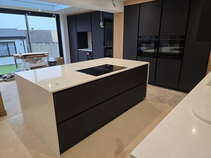 Handleless dark grey kitchen with a white quartz island and integrated ovens