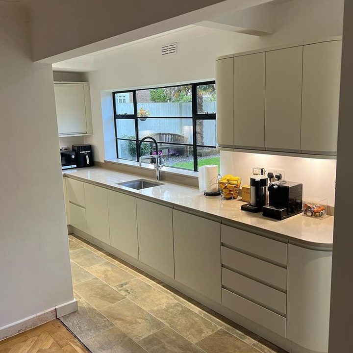 Refitted sage green kitchen with a long run of handleless units under a garden window